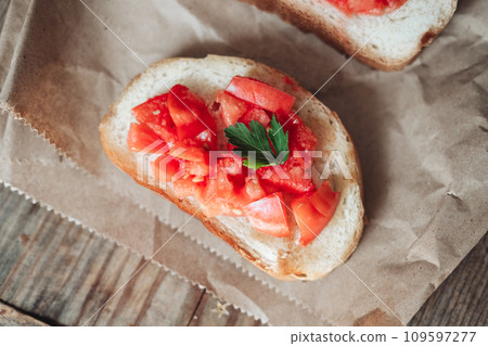 Delicious bruschetta, toasted bread with tomatoes on craft paper, on a wooden background 109597277