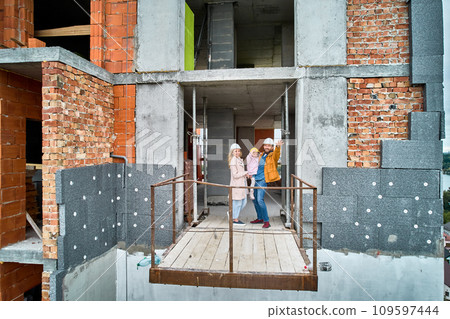Man with wife and child standing inside residential building under construction. Urban district with newly constructed apartment building and family new residents real estate buyers. Drone view 109597444