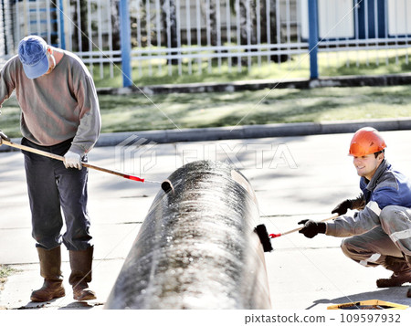 Two workers paint metal pipe black with paint rollers. Pipe treatment for corrosion protection Two workers paint metal pipe black with paint rollers. Pipe treatment for corrosion protection 109597932