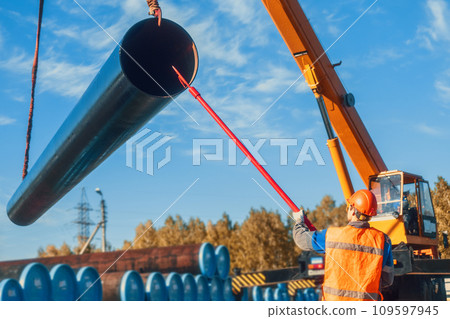 Professional slinger unloads large pipes for gasification on summer day in open warehouse. Supplier Professional slinger unloads large pipes for gasification on summer day in open warehouse. Supplier 109597945