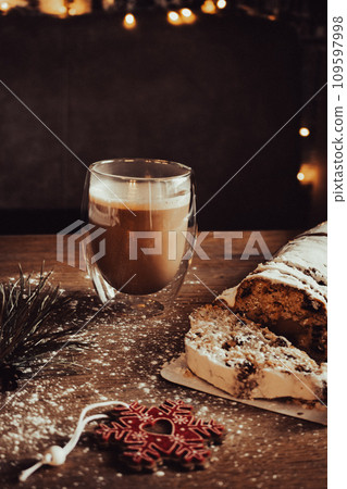 Christmas stollen with coffee cup and decoration toys. Sweet Christmas bread with cacao and powdered sugar. New Year decor. Homemade stollen with raisins on festive table. Winter breakfast.  109597998