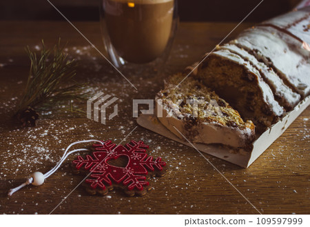 Christmas stollen with coffee cup and decoration toys. Sweet Christmas bread with cacao and powdered sugar. New Year decor. Homemade stollen with raisins on festive table. Winter breakfast.  109597999