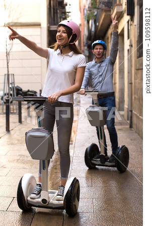 Young couple guy and girl walking on segway in streets of european city 109598112