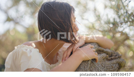 Beautiful Asian young woman in white dress outdoor near olive tree. embracing fresh air and engaging in outdoor activities. Friluftsliv concept means spending as much time outdoors as possible 109598457