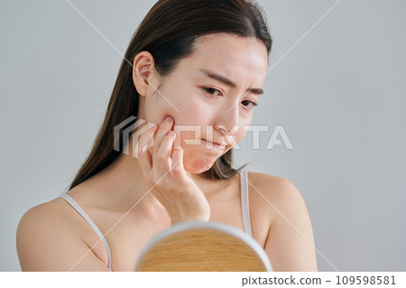 A woman in her 30s worries about wrinkles on her skin while looking in the mirror 109598581