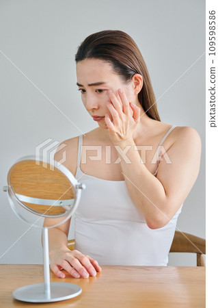 A woman in her 30s worries about wrinkles on her skin while looking in the mirror A woman in her 30s worries about wrinkles on her skin while looking in the mirror 109598586