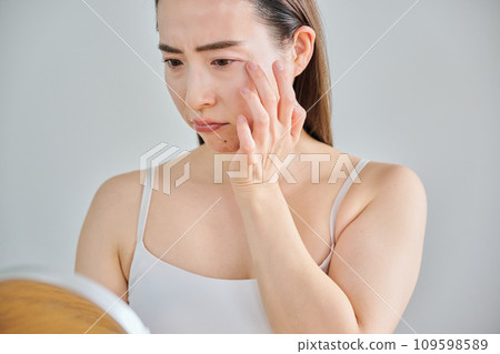 A woman in her 30s worries about wrinkles on her skin while looking in the mirror 109598589