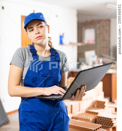 Female designer in blue overalls working with laptop in apartment under renovation Female designer in blue overalls working with laptop in apartment under renovation 109598931