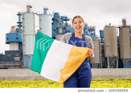 Happy young woman worker with flag of Ireland against background of factory 109598949