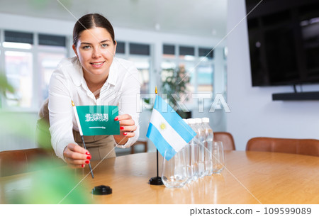 Employee of delegation prepares negotiating table - sets up flag of Saudi Aarabia and Argentine 109599089