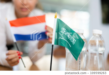 Woman secretary prepares an office for negotiations - she places flags of Saudi Arabia and Netherlands table 109599263