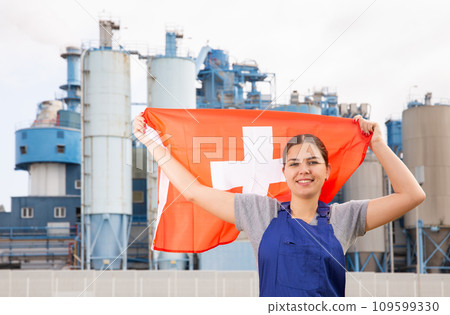 Happy young woman worker with flag of Switzerland against background of factory 109599330
