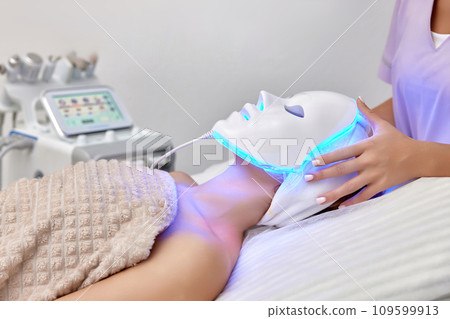 woman receiving led light anti-aging mask treatment from beautician in beauty salon 109599913
