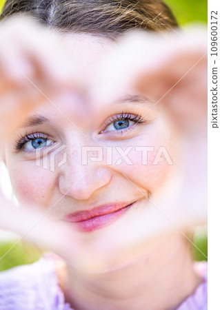 Heartfelt Gaze: Woman Framing Her Face with a Heart Shape 109600172