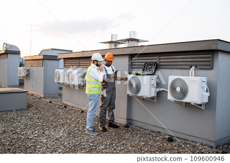 Two construction workers on roof inspecting cooling system Two construction workers on roof inspecting cooling system 109600946