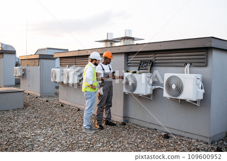 Two construction workers on roof inspecting cooling system Two construction workers on roof inspecting cooling system 109600952