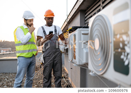 Two technicians standing with multimeter near cooling system 109600976