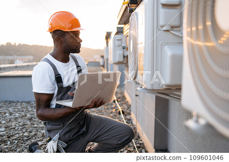 Carpenter using laptop while kneeling near air conditioner Carpenter using laptop while kneeling near air conditioner 109601046
