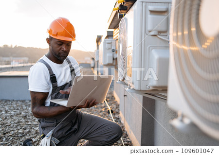Carpenter using laptop while kneeling near air conditioner 109601047