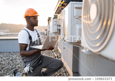 Male kneeling with laptop near hanging air conditioner 109601071