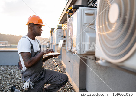 Male kneeling with laptop near hanging air conditioner Male kneeling with laptop near hanging air conditioner 109601080
