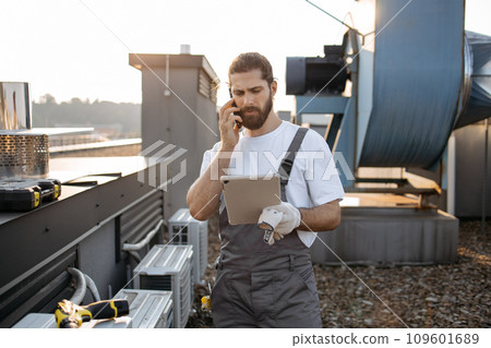 Man factory worker using tablet and talking on phone on roof 109601689