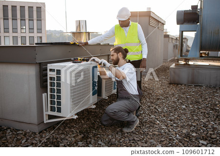 Diverse plant workers repairing air conditioner on rooftop 109601712