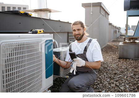 Builder man applying voltage tester to conditioner outdoor 109601786