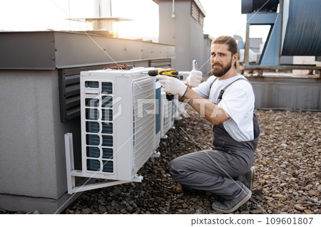 Male worker repairing conditioner while using drill outdoor 109601807