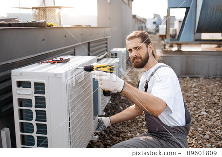 Craftsman using drill while repairing conditioner on roof 109601809