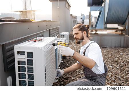 Craftsman using drill while repairing conditioner on roof Craftsman using drill while repairing conditioner on roof 109601811