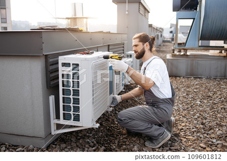 Craftsman using drill while repairing conditioner on roof Craftsman using drill while repairing conditioner on roof 109601812