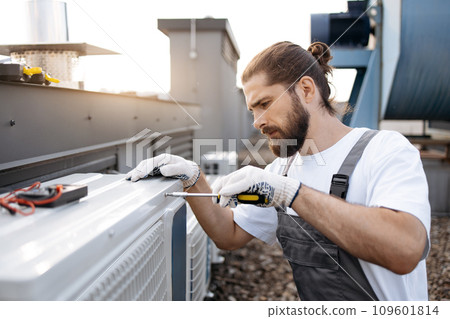 Repairman fixing conditioner using screwdriver on roof 109601814