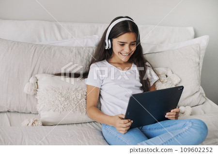 Preteen girl wear headphones using modern digital tablet at home 109602252
