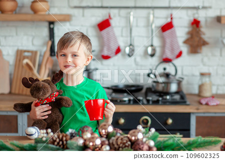 Cute little boy eating Christmas cookies and drinking a drink in Christmas decorations in the kitchen. 109602325