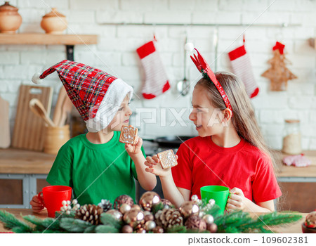 Brother and sister, little boy and girl eating Christmas cookies and drinking drink in Christmas decorations in the kitchen. Brother and sister, little boy and girl eating Christmas cookies and drinking drink in Christmas decorations in the kitchen. 109602381