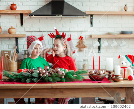 Brother and sister, little boy and girl eating Christmas cookies and drinking drink in Christmas decorations in the kitchen. 109602402