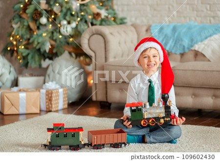 Happy little boy with a gift, toy train, under the Christmas tree on New Year's morning. Time to fulfill wishes. 109602430