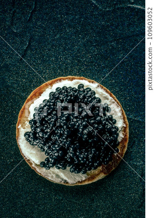 A blini with caviar and cream cheese, shot from the top on black 109603052