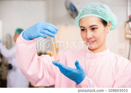 Within juice beverage factory woman food engineer illustrates food and beverage quality and safety testing using test tubes for sampling basil or chia seeds in bottled products emphasizing expertise 109603055