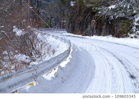 Downhill S-shaped road covered with snow in the mountains in winter Downhill S-shaped road covered with snow in the mountains in winter 109603345