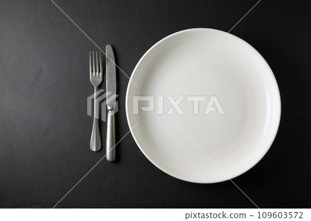 Empty white dinner plate and cutlery on a black stone table. Top view with copy space Empty white dinner plate and cutlery on a black stone table. Top view with copy space 109603572