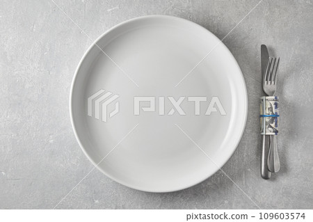 Empty white dinner plate and cutlery wrapped in a hundred dollar bill on a gray stone table. Top view with copy space Empty white dinner plate and cutlery wrapped in a hundred dollar bill on a gray stone table. Top view with copy space 109603574