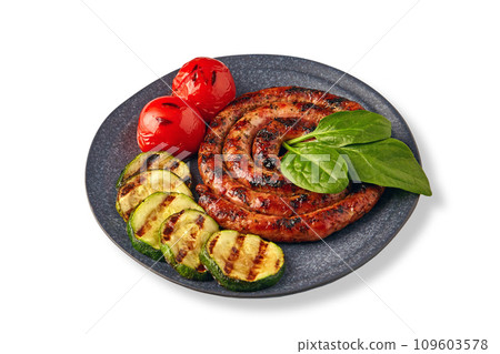 Fried spiral sausage with grilled vegetables and basil on a ceramic plate isolated on a white background 109603578