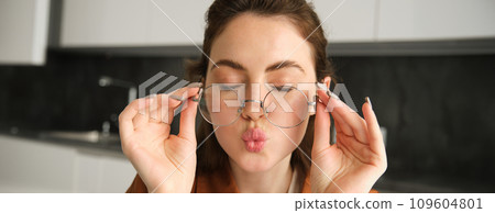 Close up portrait of happy, carefree young woman in her new glasses, showing her eyewear, laughing and smiling, posing in kitchen 109604801
