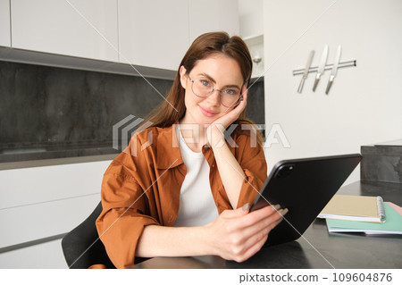 Portrait of cute woman, student in glasses, sitting in kitchen with digital tablet, working remotely, making home as workplace, teacher giving lessons online 109604876