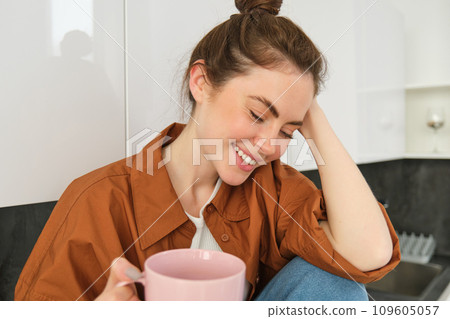 Cosy moments. Happy young woman sits in kitchen and drinks coffee, has tender smile on her face Cosy moments. Happy young woman sits in kitchen and drinks coffee, has tender smile on her face 109605057
