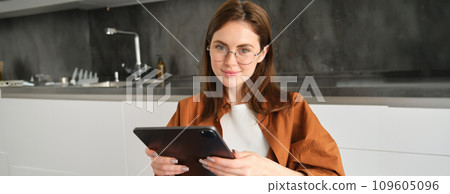 Portrait of busy young woman, self-employed entrepreneur sitting at home with digital tablet, reading documents. Student working on project remotely, holding gadget, studying Portrait of busy young woman, self-employed entrepreneur sitting at home with digital tablet, reading documents. Student working on project remotely, holding gadget, studying 109605096