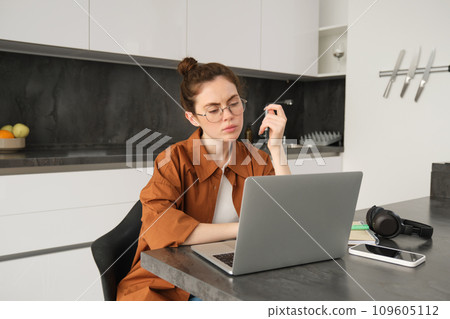Portrait of woman with serious face, sitting in front of computer, using laptop, working from home, looking at screen with thoughtful face 109605112