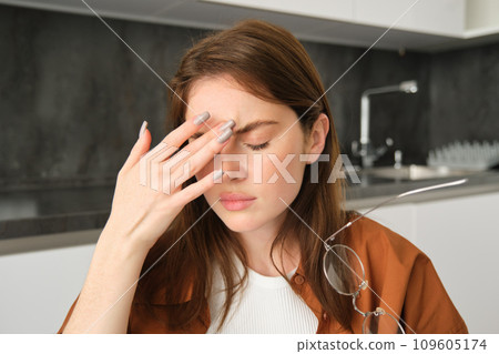 Close up portrait of brunette woman touching head, feeling unwell, has headache or migraine, sitting in kitchen with dizziness. 109605174